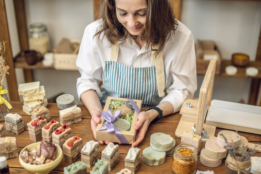 Woman soap maker in a workshop is packing in the gift box handmade natural soap. Cozy creative atmosphere and nice hobby