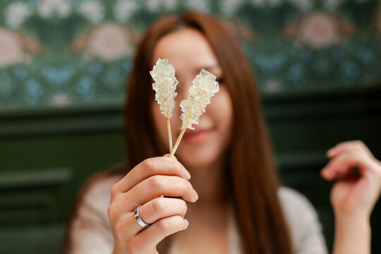 Closeup of woman holding stick of rock candies on a wooden stick