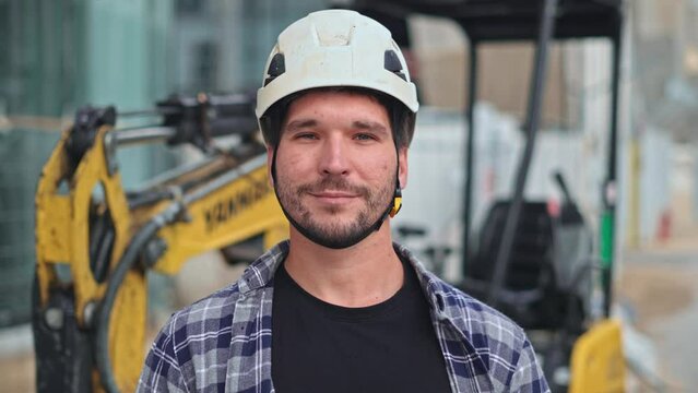 Confident construction site worker portrait. Smile constructor man look at camera. Builder engineer wear white helmet. Excavator driver plaid shirt. Guy build new house city street. Erector person job