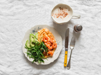 Delicious breakfast, brunch - omelette, shrimp, avocado, arugula salad and cappuccino on a light background, top view