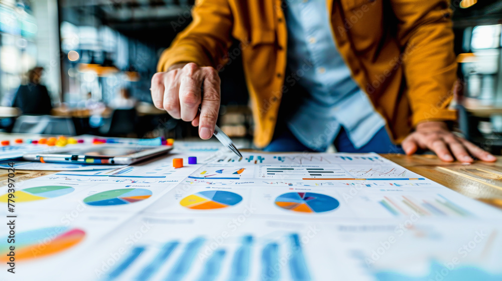 Poster person in business attire analyzing colorful charts and graphs on paper with a pen, possibly in a co