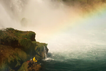 Fisherman in bright yellow raincoat fishing from a rock right next to the Düden Waterfalls in...