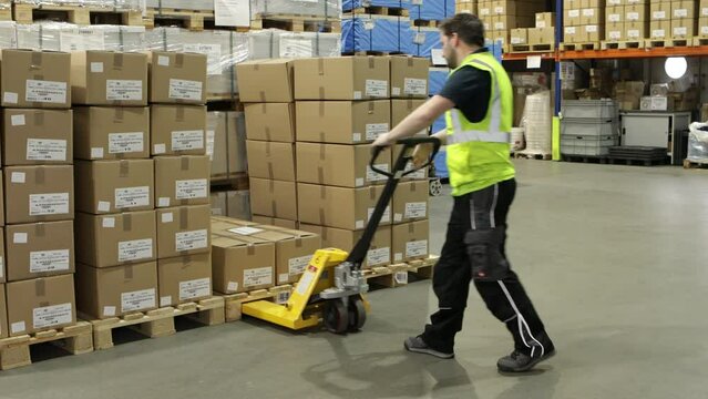 Warehouse interior with stacked boxes on pallets, yellow pallet jack in aisle, fluorescent lighting