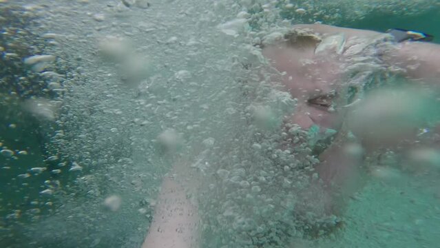 Man submerged underwater, surrounded by bubbles, then surfacing In The Kali Biru (Blue River) Within Tropical Forest in Raja Ampat, West Papua, Indonesia.