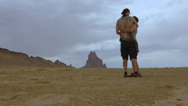Two traveling lovers embrace in the desert at Shiprock in New Mexico