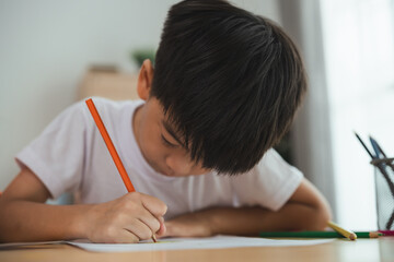 A young boy is sitting at a desk and writing with a pencil. He is focused on his work and he is in a serious mood. Concept of a child learning and practicing their writing skills