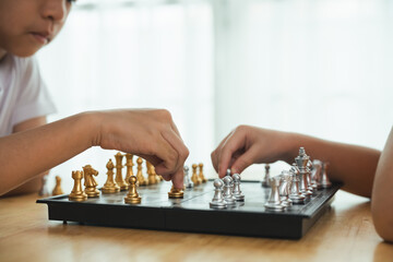 Two children playing a game of chess. One of the children is wearing a white shirt. The game is being played on a black and white board - Powered by Adobe