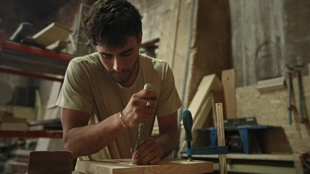 Young man carpenter carving wood block. Guy process timber bar. Male carpentry work skill. Joiner woodwork. Worker beat hammer. Person use chisel. Diy master class workshop Woodworker make job project