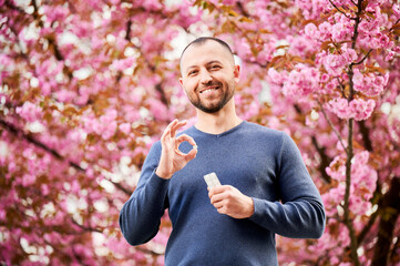 Man allergic suffering from seasonal allergy in blossoming garden at spring. Handsome smiling man...