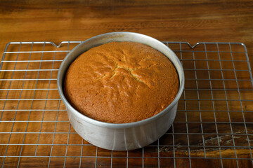 Freshly baked sponge cake cooling on wooden table.