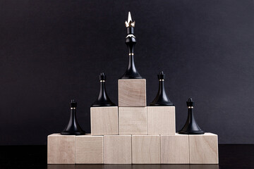 Chess figures on a toy wooden ladder - a chess pawns on the bottom and a chess queen on top,...