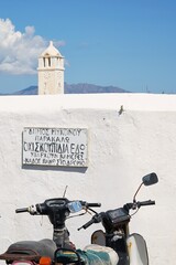 Motorbikes resting below a hand-painted Greek parking sign with a view of the mountains visible in the distance on the island of Mykonos, Greece