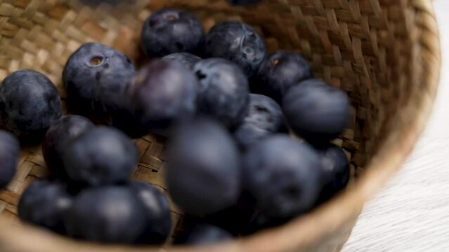 Fresh blueberries falling into a rustic wicker bowl in slow motion. Delicious organic blue bilberry close up. Rural style view