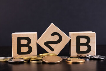 Cubes with word B2B and stacked coins on wooden surface