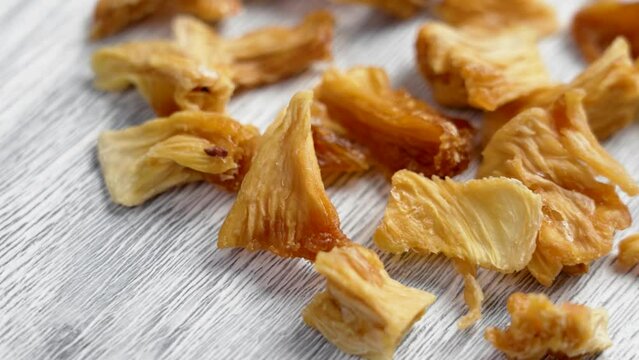 Sweet dried pineapple slices on a white textured board close up. Healthy fruity natural snacks. Rotation