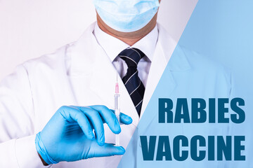 Rabies Vaccine text is written on the background of a doctor who is holding a syringe with a vaccine in a medical mask and gloves. Medical concept.