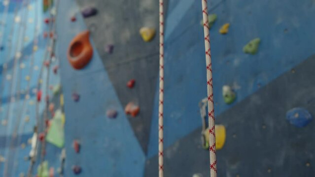 Tilt up shot of rope in indoor climbing gym in front of wall with holds. Close up view with focus on foreground