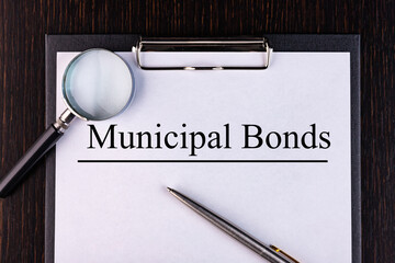 Text MUNICIPAL BONDS is written on a notebook with a pen and a magnifying glass lying on the table....