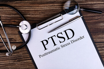 PTSD text is written on a tablet lying on a dark table with a stethoscope and a magnifying glass....