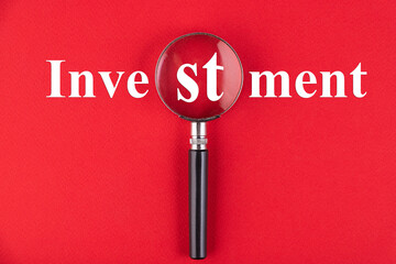 INVESTMENT text written through a magnifying glass on a red background. Business education concept.