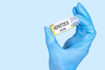 HEPATITIS B VACCINE text is written on a vial whose ampoule is held by a hand in a medical...
