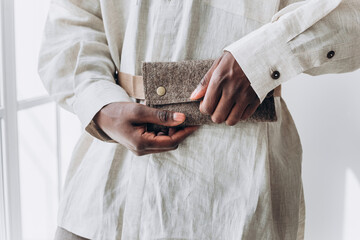 Close-Up of African American Man's Hands Holding a Textured Wallet. Close-up of a person's hands fastening a stylish felt wallet, showcasing a blend of practicality and fashion in soft natural - obrazy, fototapety, plakaty