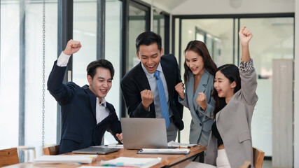 A vibrant team of four celebrates a business victory with raised fists and joyful expressions at...