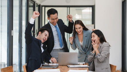 Enthusiastic office workers experience a moment of triumph, sharing success around a laptop in office.