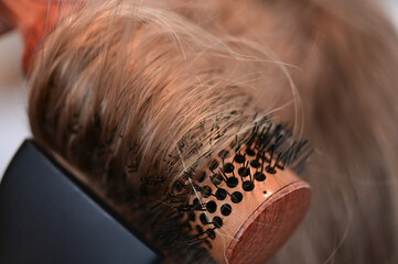 Close up of a blonde woman getting styled with a hair brush and hairdryer