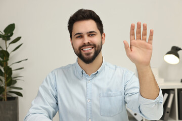 Happy young man waving hello during video chat indoors, view from web camera © New Africa