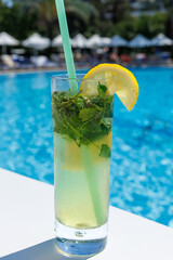 Mojito cocktail at the edge of a resort pool. Concept of luxury vacation. Outdoor pool background. Vertical