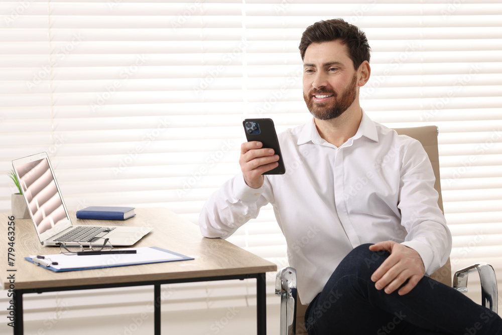Poster smiling man using smartphone at table in office