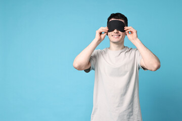 Happy man in pyjama and sleep mask on light blue background, space for text