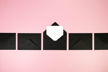 Top view of black envelopes, white card on pink background. Post flat lay. Copy space.