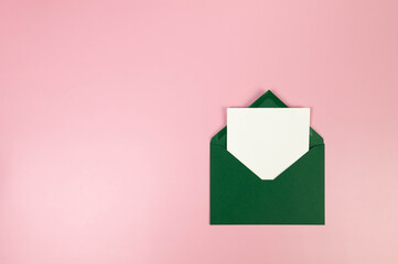 Top view of dark green envelope, white card on pink background. Post flat lay. Copy space.