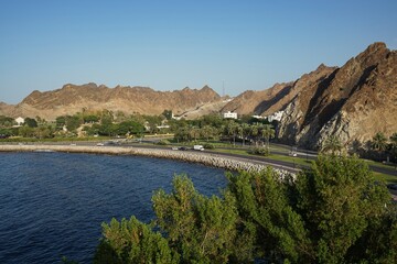 Warm landscape view of the Hajar mountains and ocean-side boulevard along the Persian Gulf in Muscat, Oman