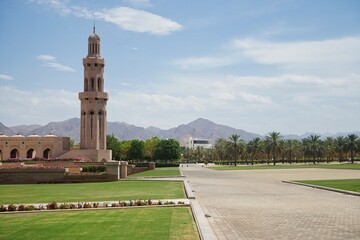 Decorated tower and lush manicured gardens of the Sultan Qaboos Grand Mosque, with the Hajar mountains visible in the distance, in Muscat, Oman