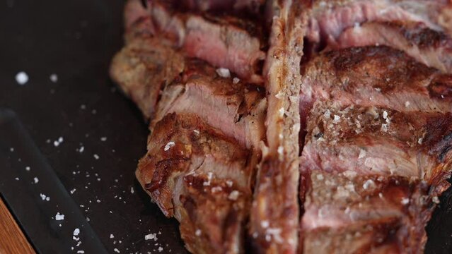 T-bone steak. 4K close up video with a beef t-bone steak on a black platter with spread salt around it. Beef barbecue grill video.
