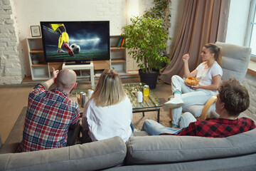 Friends, sport fans meeting at home, sitting on couch in living room on daytime and watching online...