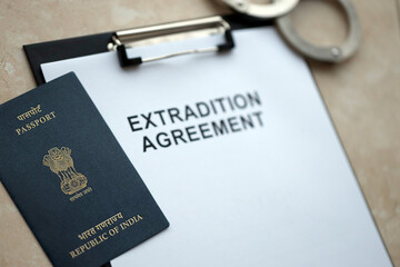 Passport of India and Extradition Agreement with handcuffs on table close up