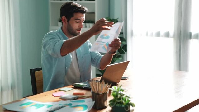 Professional smart manager working on laptop while looking at data analysis. Leader compare financial statistic graph while making decision at meeting table with document scatter around. Convocation.