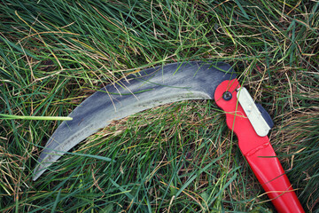 The small grass scythe for gardening. Mow with manual metallic sharp blade on the green lawn.