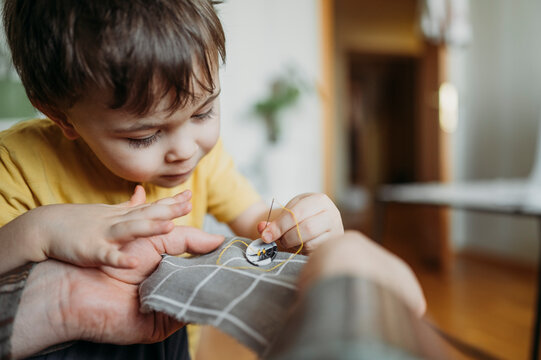 Father teaching son to sew button on gray colored cloth