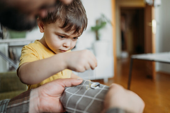 Father teaching son to sew button on gray colored cloth at home