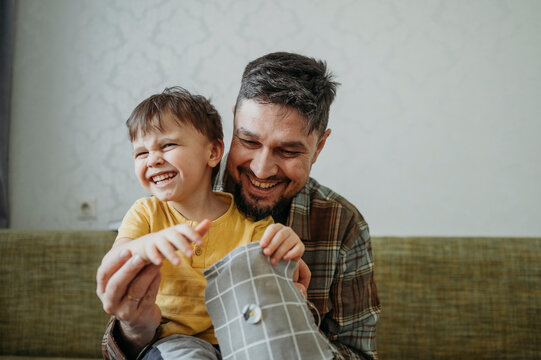 Happy father teaching son to sew button on gray colored cloth at home