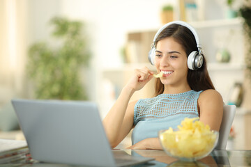 Happy woman eating snack and watching movie on laptop - Powered by Adobe