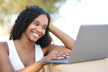 Happy black woman using laptop watching online content outdoors