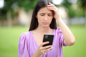 Worried woman checking bad news on smart phone in a park