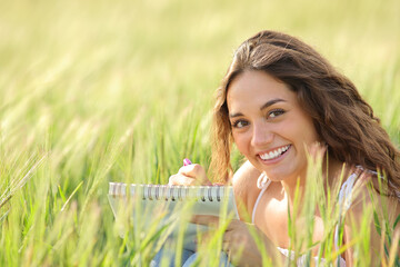Happy woman drawing in a field looking at you