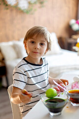 Beatiful blond child, boy, coloring and painting eggs for Easter at home